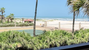 Blick auf einen Strand mit Palmen, einem Tennisplatz und einem Gebäude mit rotem Dach.