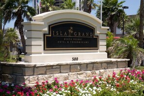 Schild für Isla Grand Beach Resort Hotel & Condominiums, mit Steinunterbau und Blumenarrangement im Vordergrund.