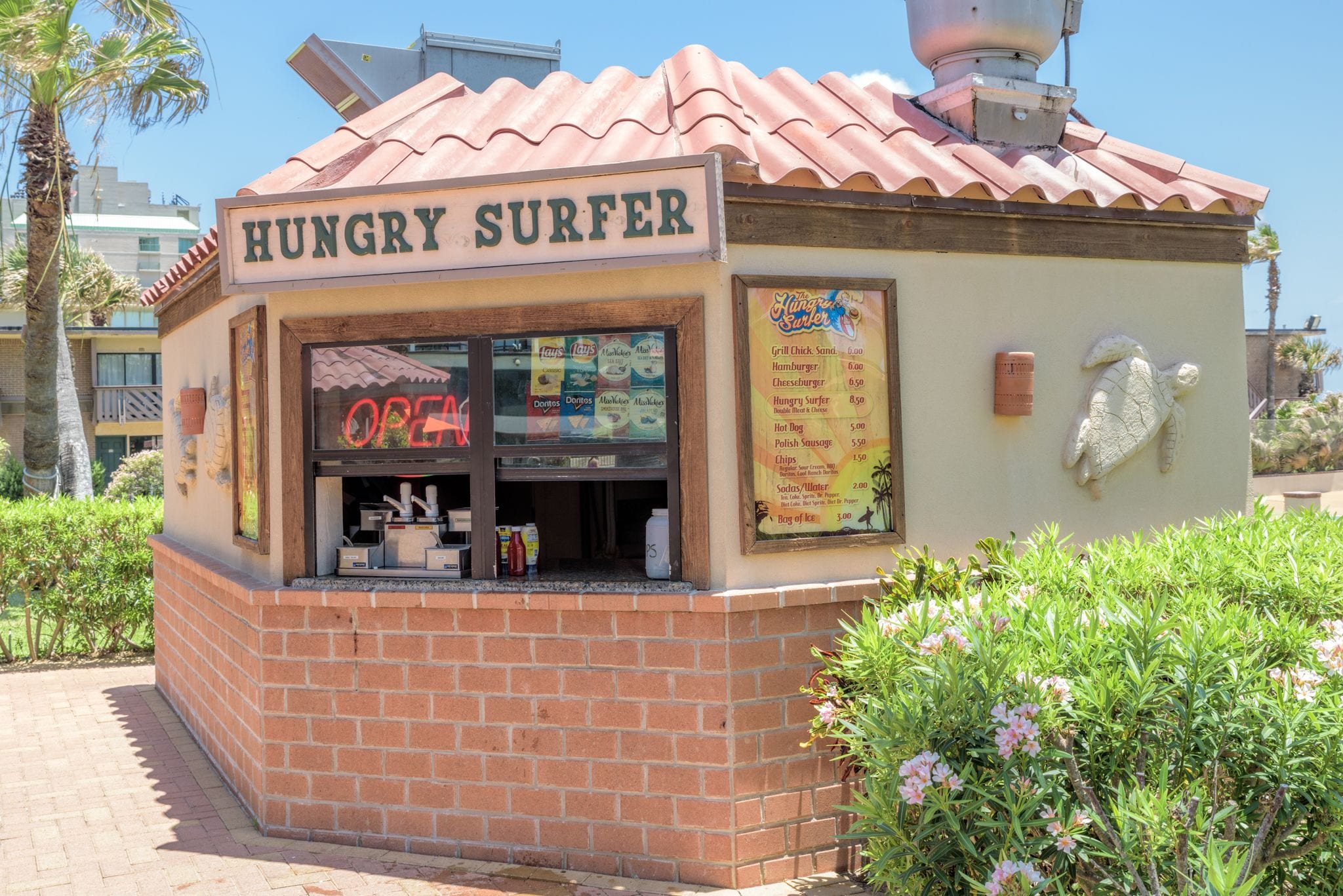 A small brick kiosk with a sign reading "Hungry Surfer" and a menu board listing food items.