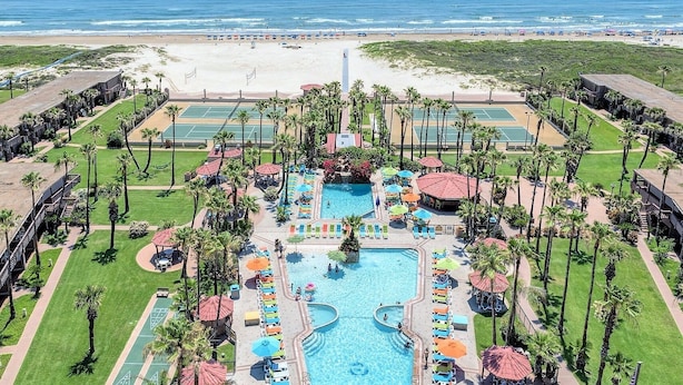 Ein Resort mit einem zentralen Pool, mehreren Tennisplätzen und Blick auf den Strand.