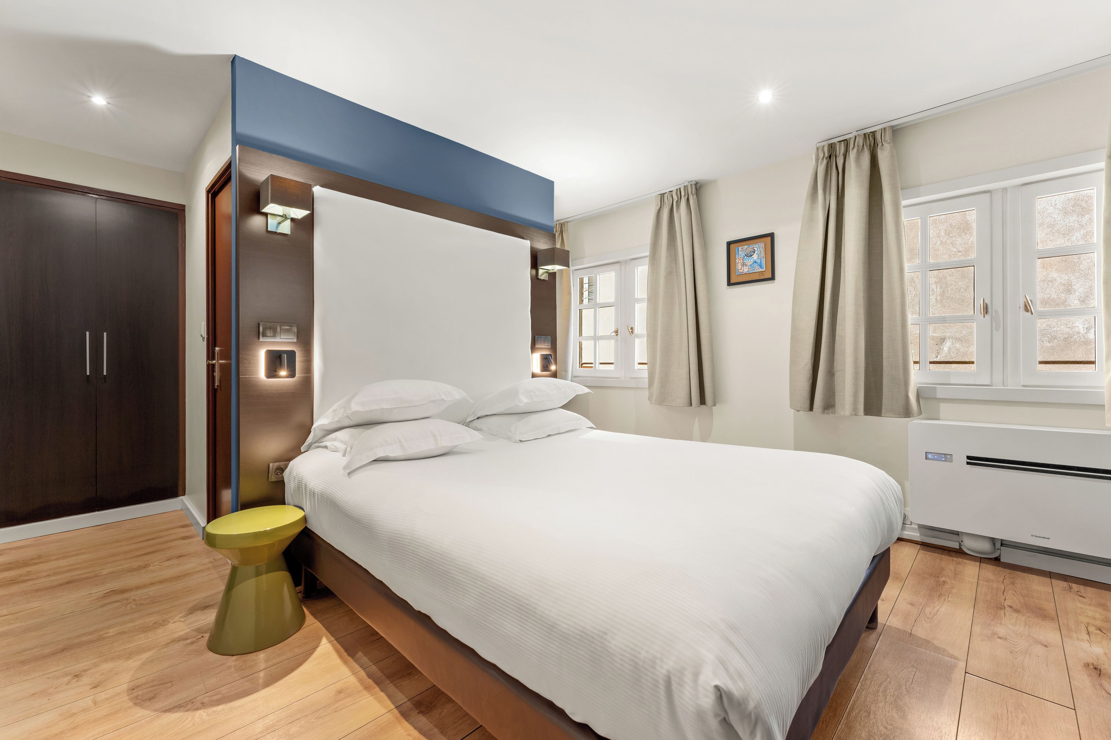 A modern hotel room with a large bed, a wardrobe, a toilet, and a window with curtains.