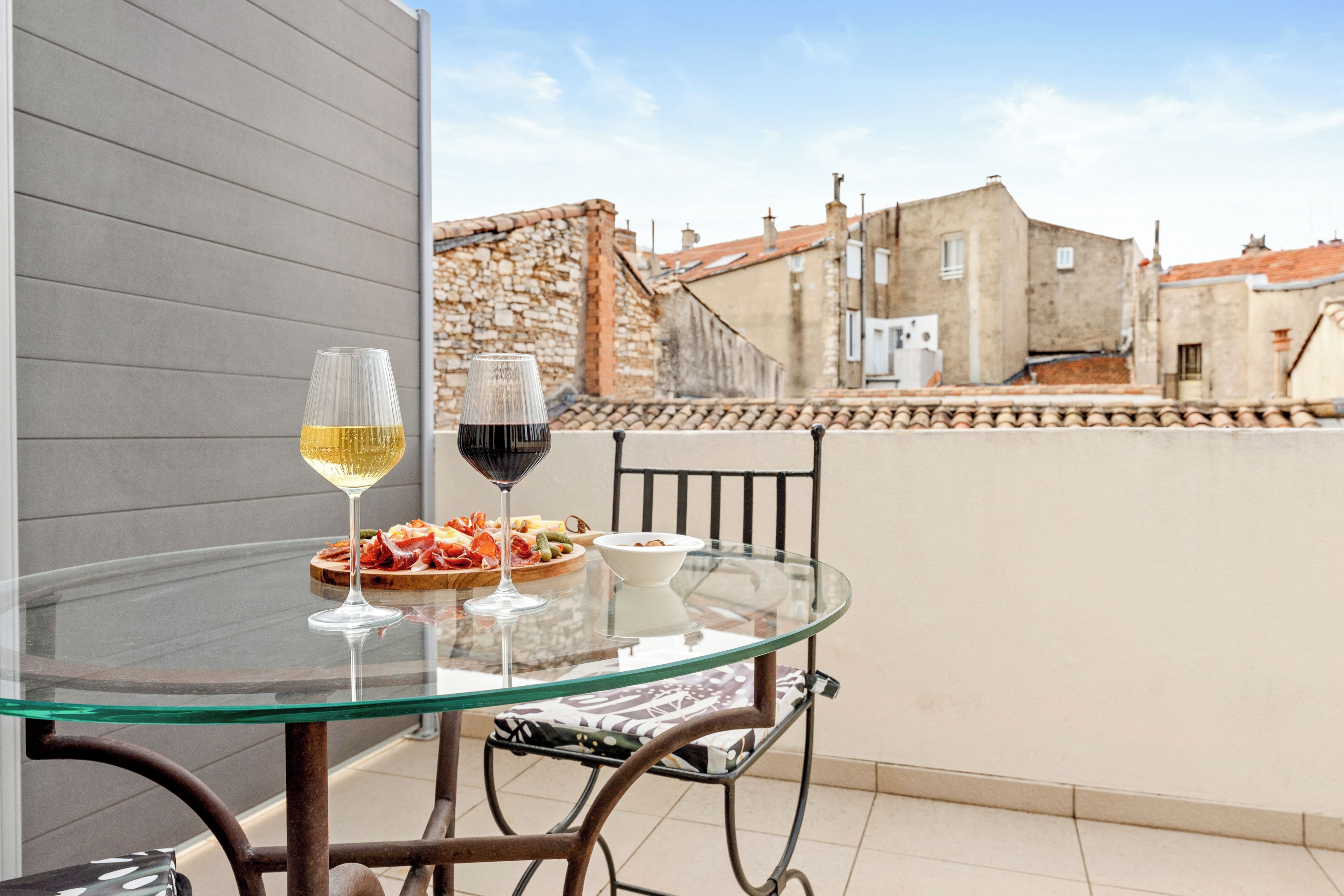 A glass table with a wine glass and a plate of food on a balcony.