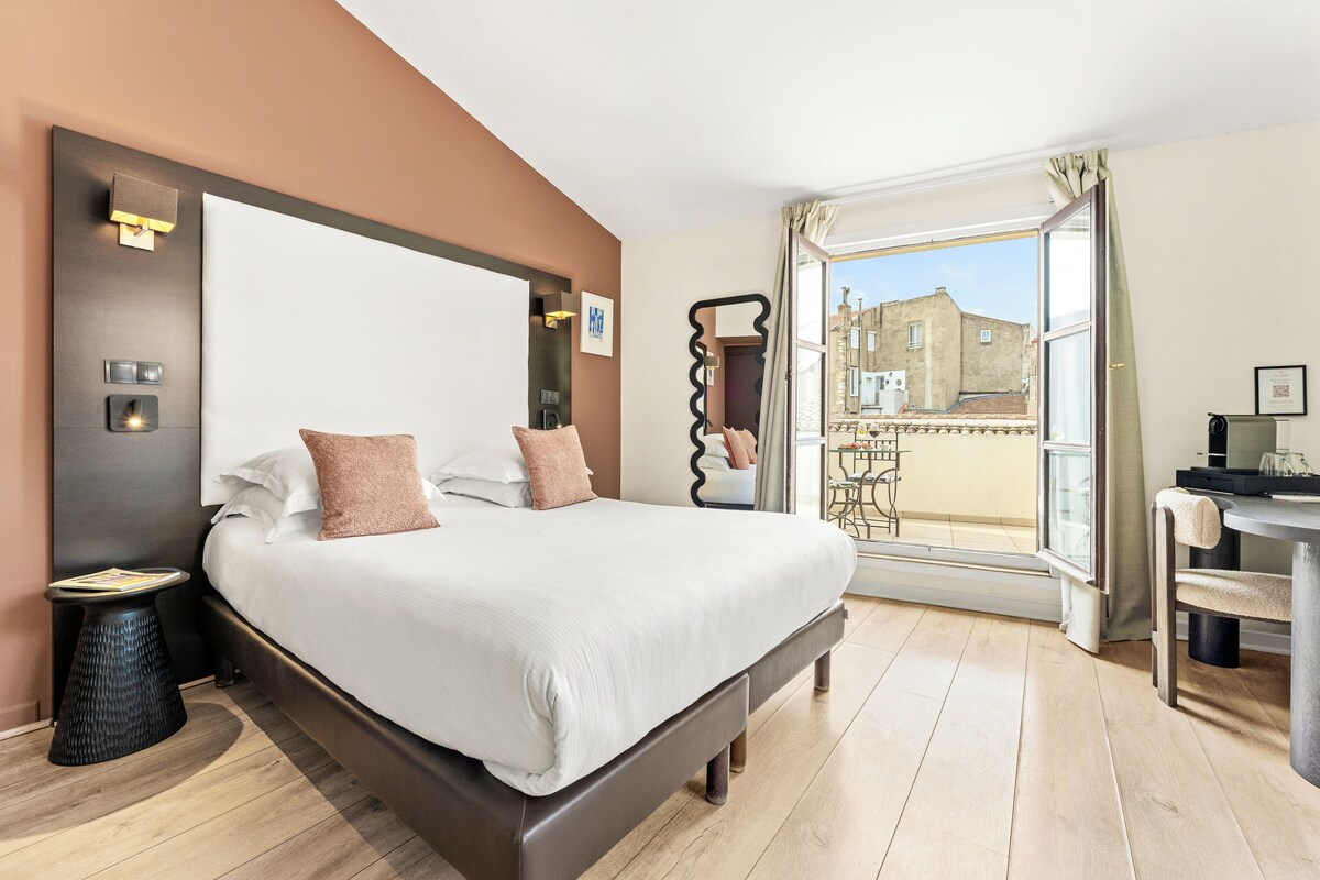 Habitación de hotel con una cama grande, un escritorio, una silla, un balcón con vistas y una puerta.