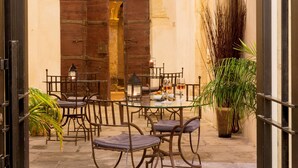 An outdoor dining area with metal chairs and tables, potted plants, and a stone wall.