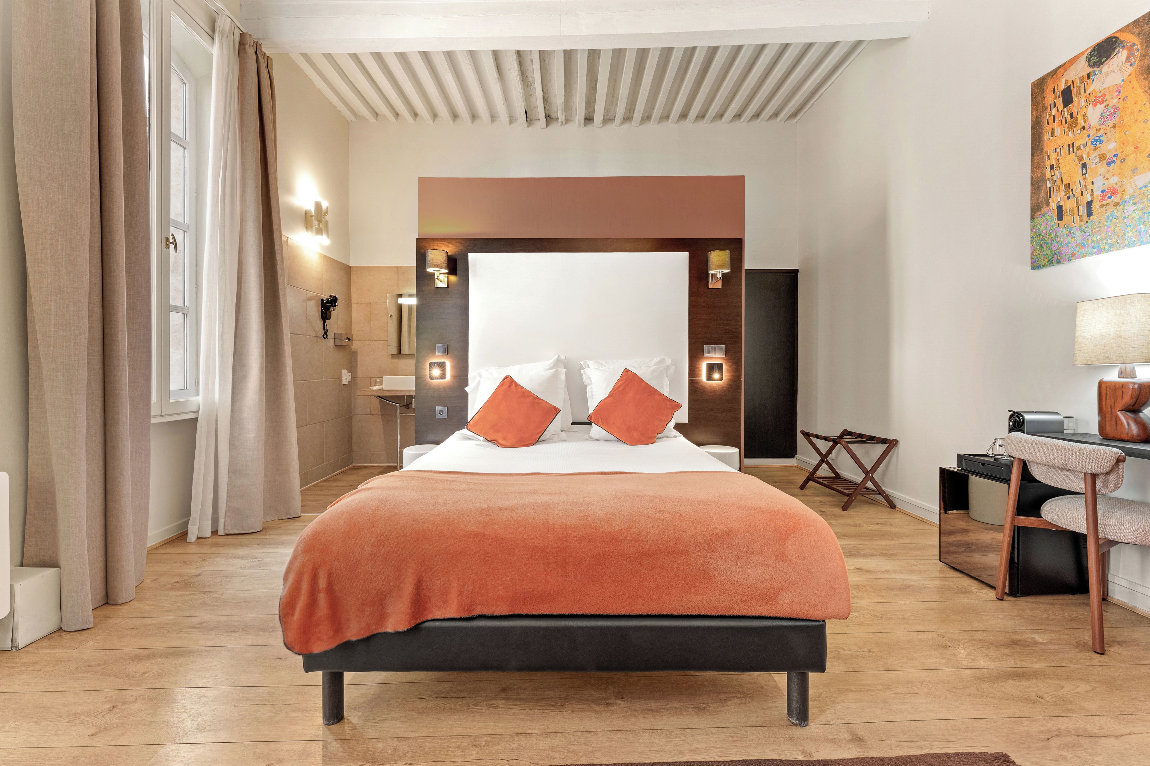 A modern bedroom with a large bed, a desk, and a bathroom in the background.