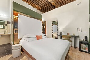 A hotel room with a bed, bedside table, mirror, and a small desk with a coffee machine.