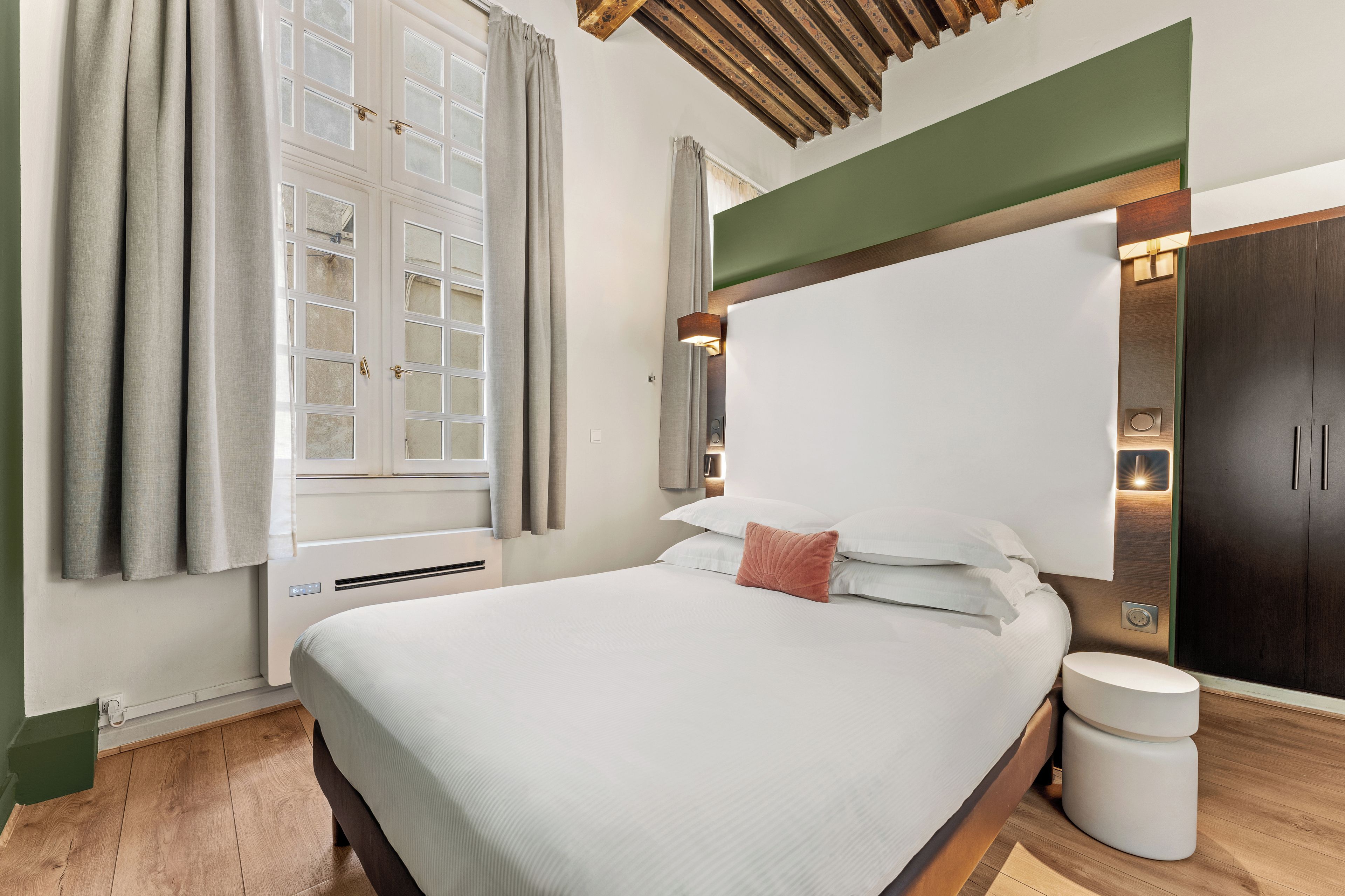 A hotel room with a bed, a bedside table, a wardrobe, and a window with curtains.
