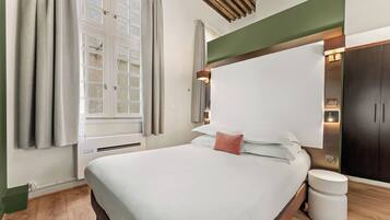 A hotel room with a bed, a bedside table, a wardrobe, and a window with curtains.
