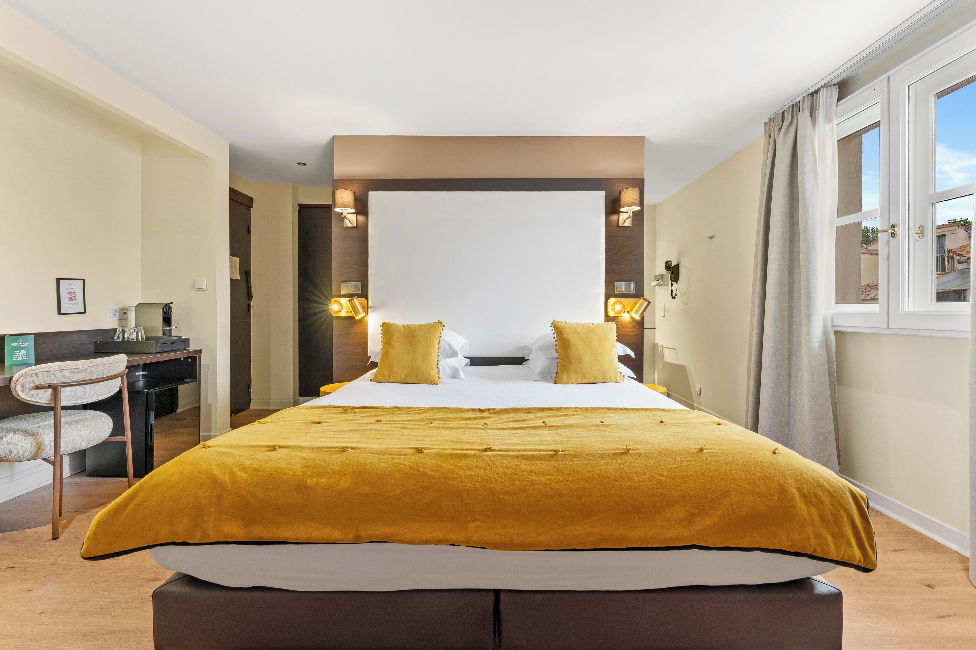 A hotel room with a large bed, two bedside lamps, a desk with a chair, and a window with curtains.