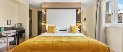 A hotel room with a large bed, two bedside lamps, a desk with a chair, and a window with curtains.