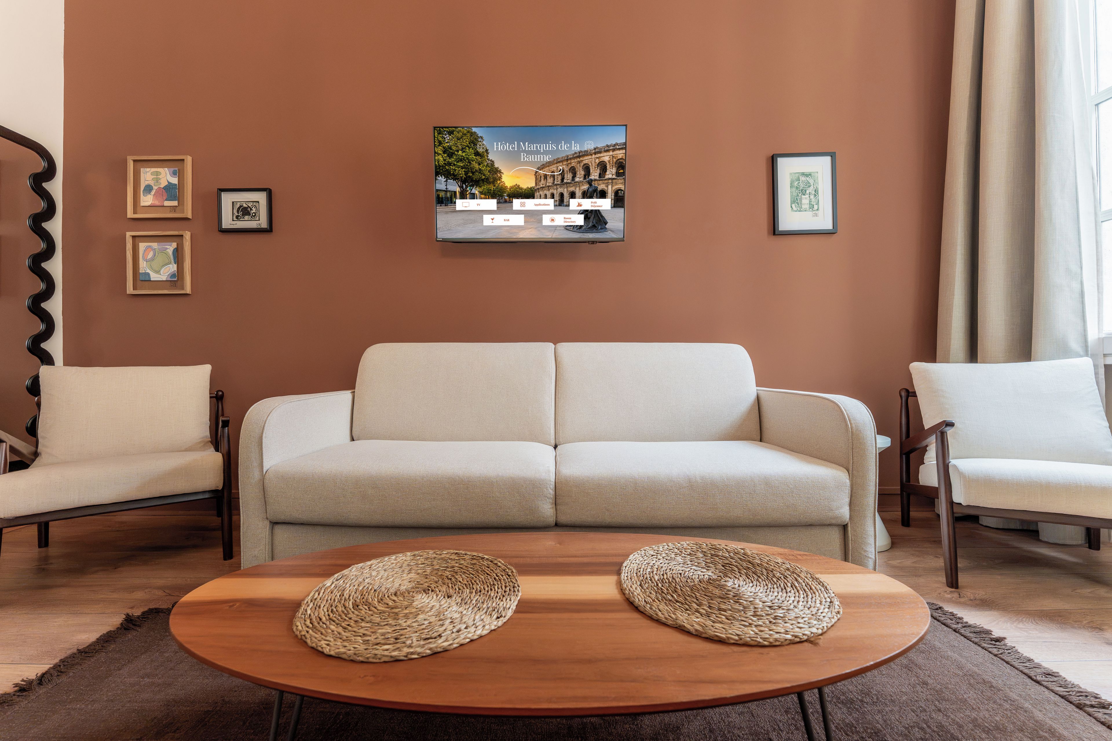 A living room with a sofa, two armchairs, a coffee table with woven placemats, and a framed picture of a building on the wall.