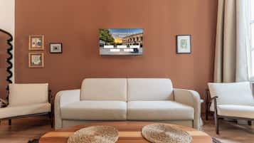 A living room with a sofa, two armchairs, a coffee table with woven placemats, and a framed picture of a building on the wall.
