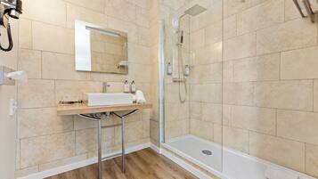 Un baño moderno con cabina de ducha de vidrio, un lavamanos blanco y un espejo encima.