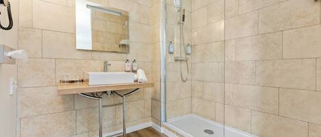 Un baño moderno con cabina de ducha de vidrio, un lavamanos blanco y un espejo encima.
