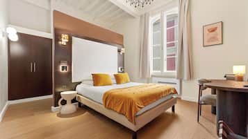 A modern bedroom with a large bed, bedside lamps, a desk, and a view of buildings through the window.
