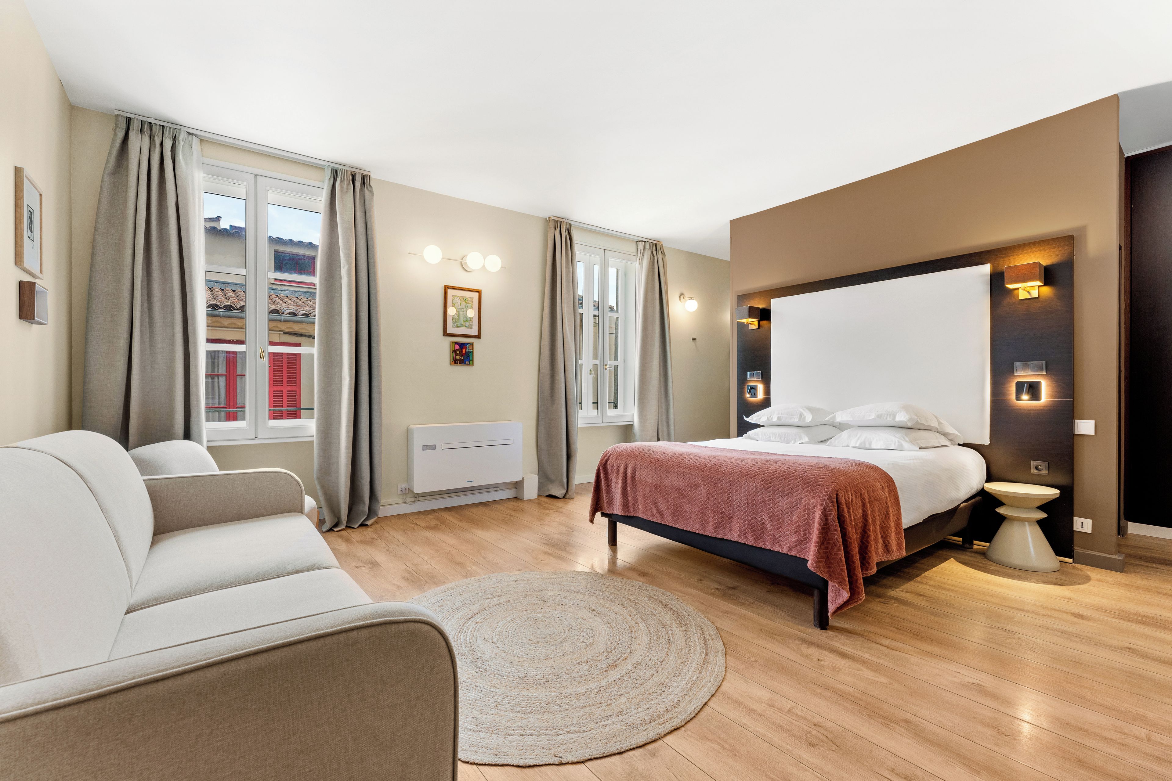 A modern bedroom with a bed, a sofa, a round rug, and a wall-mounted light fixture.