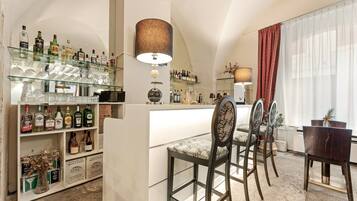 A bar area with a glass shelf stocked with bottles and glasses, a bar counter, and two upholstered chairs.