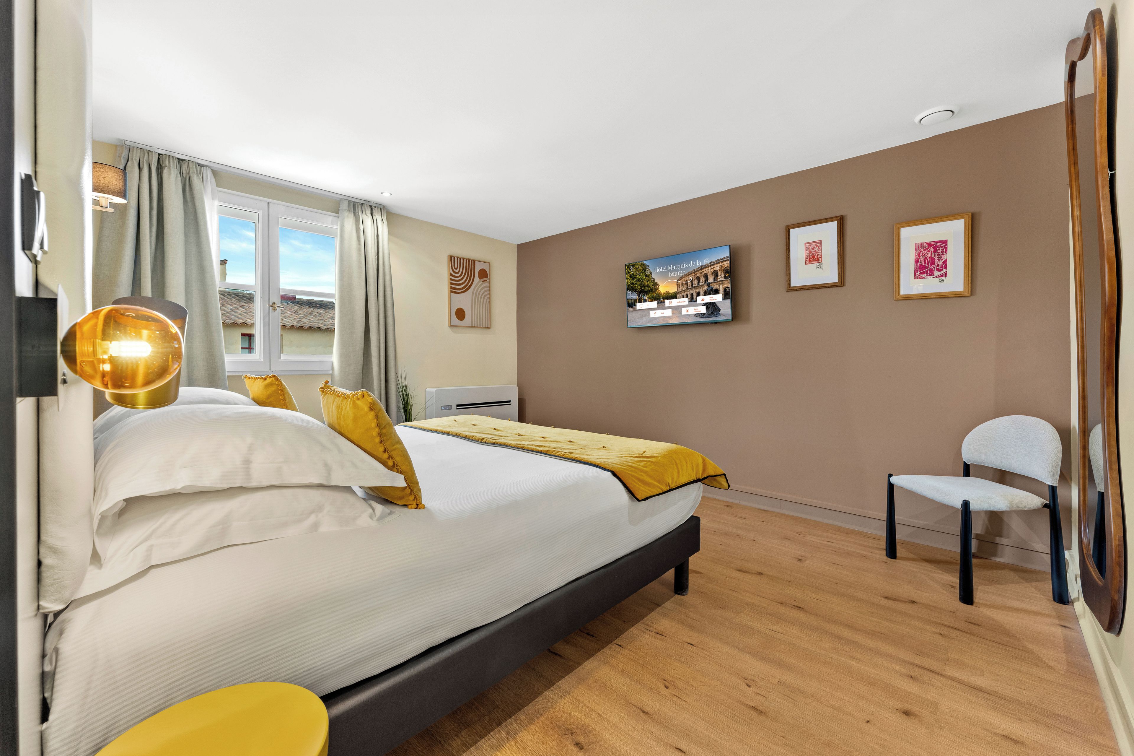 Une chambre d’hôtel avec un lit, une chaise, un bureau et une fenêtre avec des rideaux.