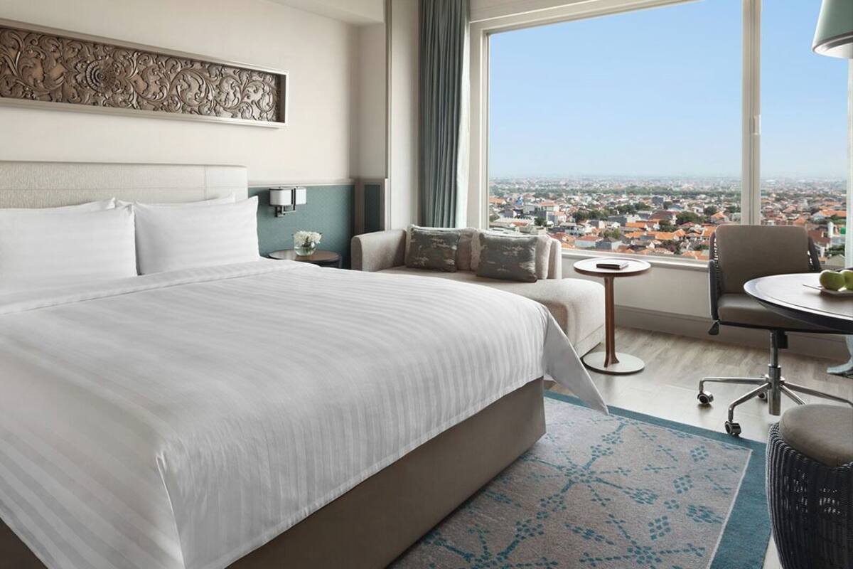 Een hotelkamer met een groot bed, een sofa, een klein tafeltje en uitzicht op de stad.