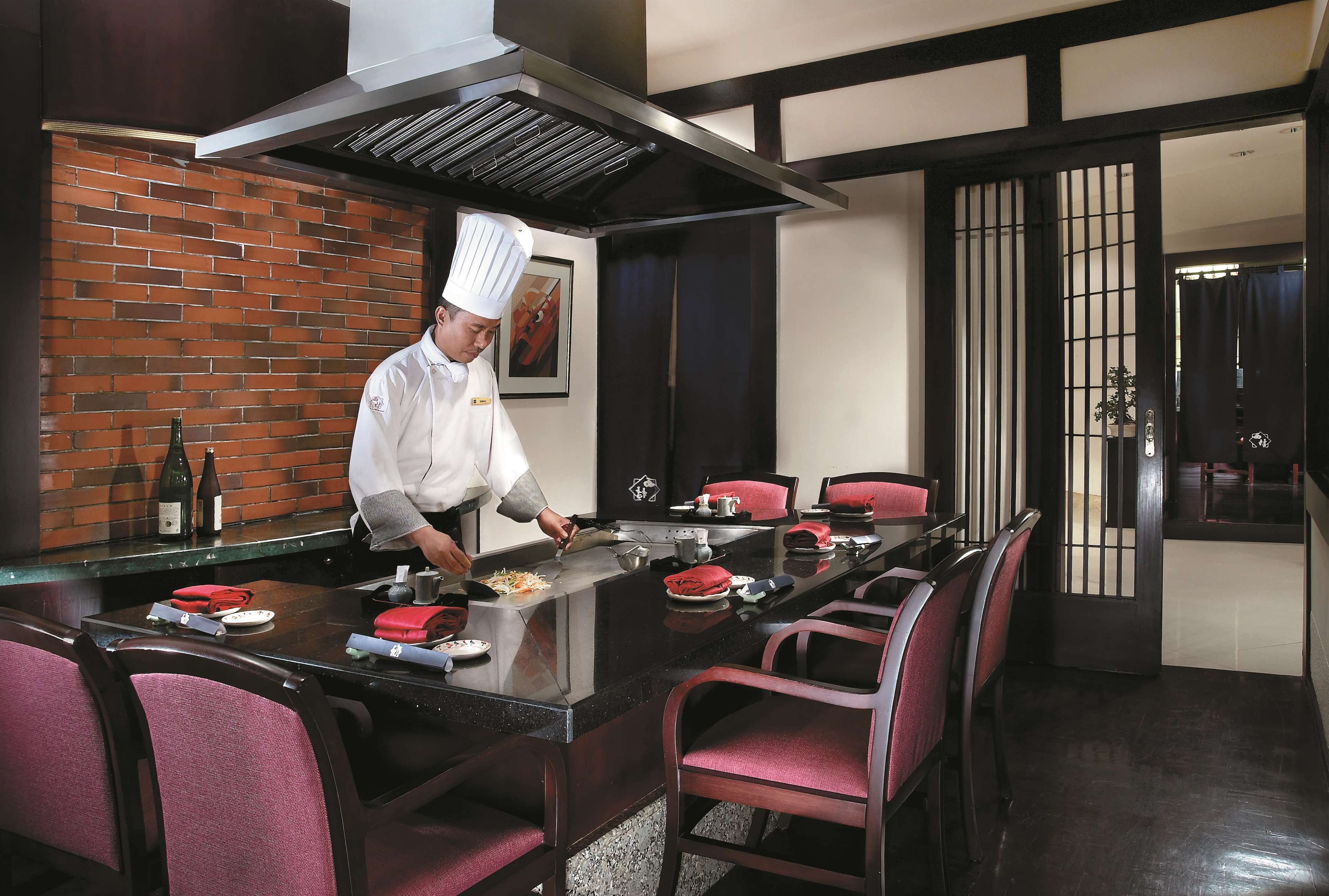 A chef preparing food at a long table in a restaurant with a brick wall and traditional sliding doors.