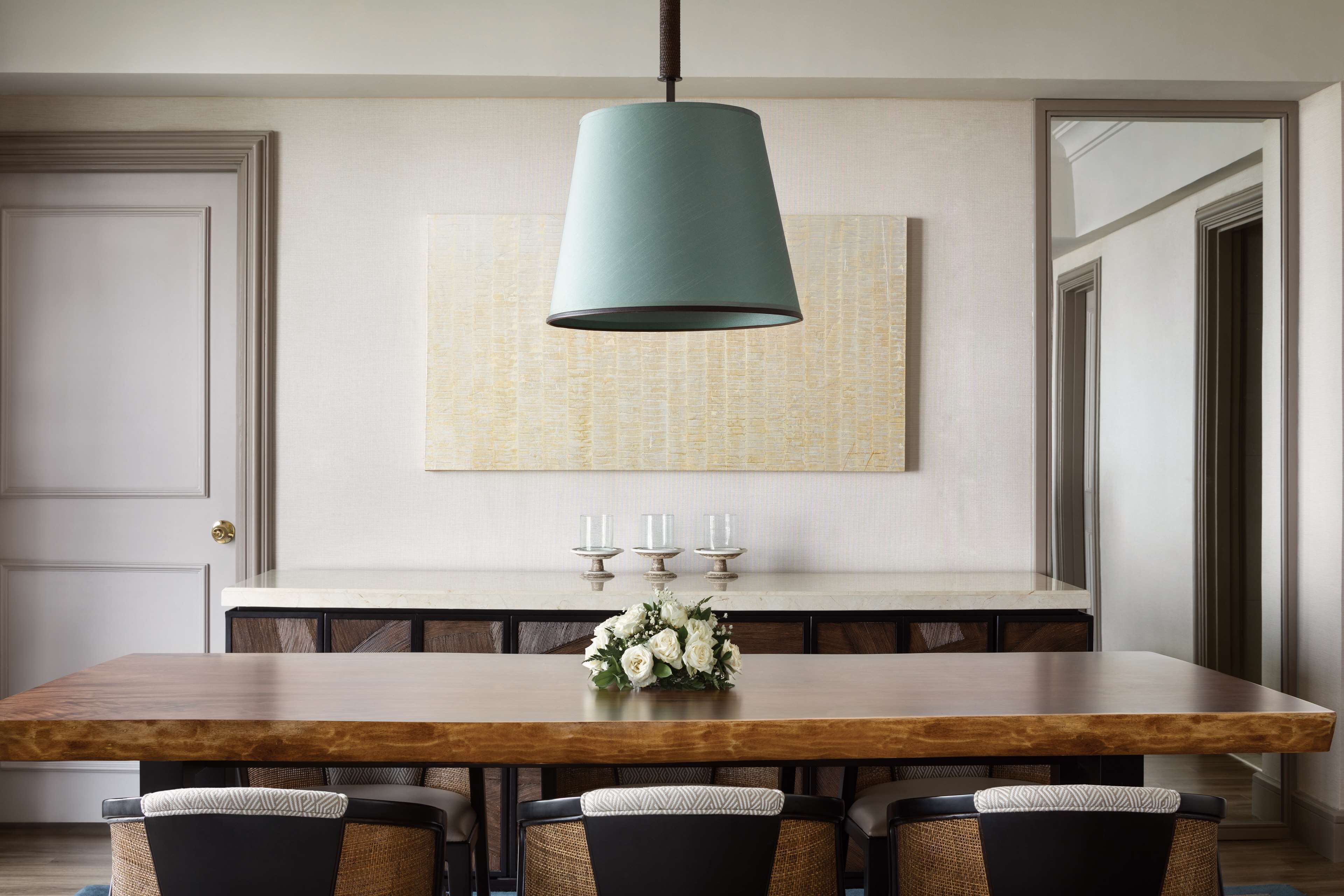 Un comedor con mesa de madera, cuatro sillas, una lámpara colgante y un arreglo floral decorativo.