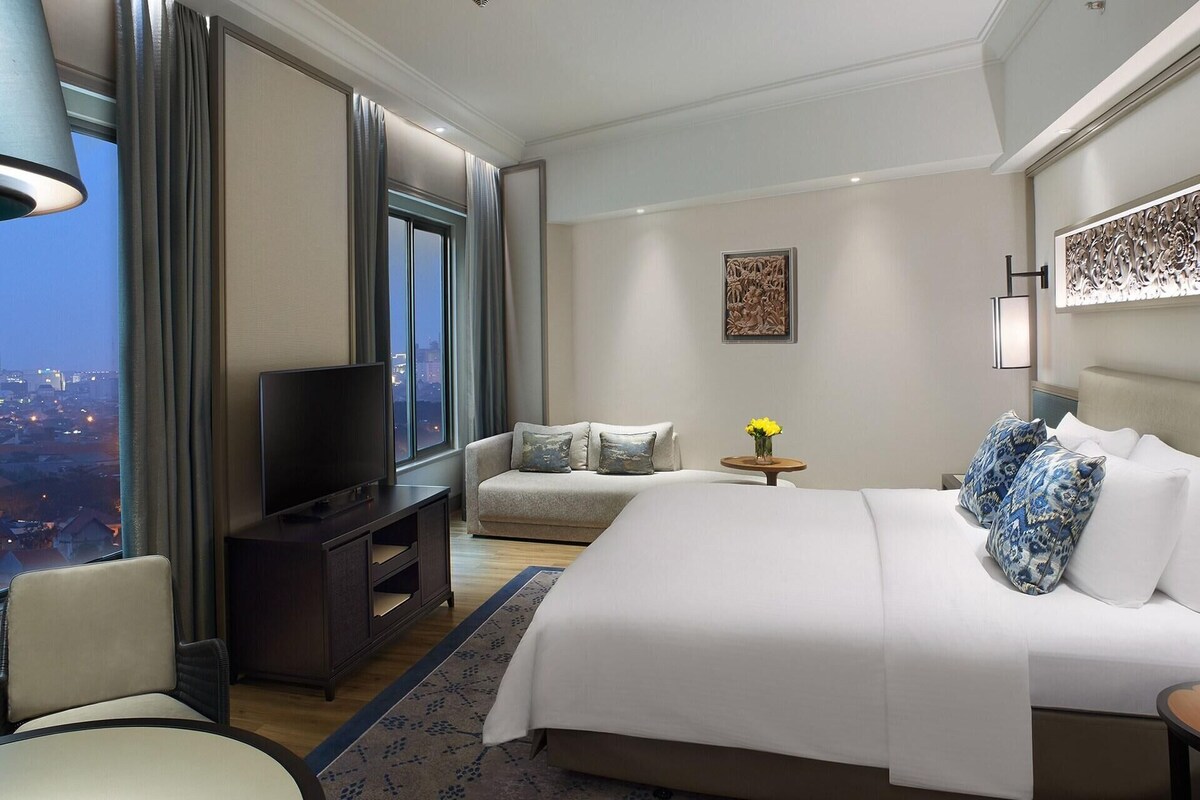 A hotel room with a large bed, a TV, a sofa, and a desk.