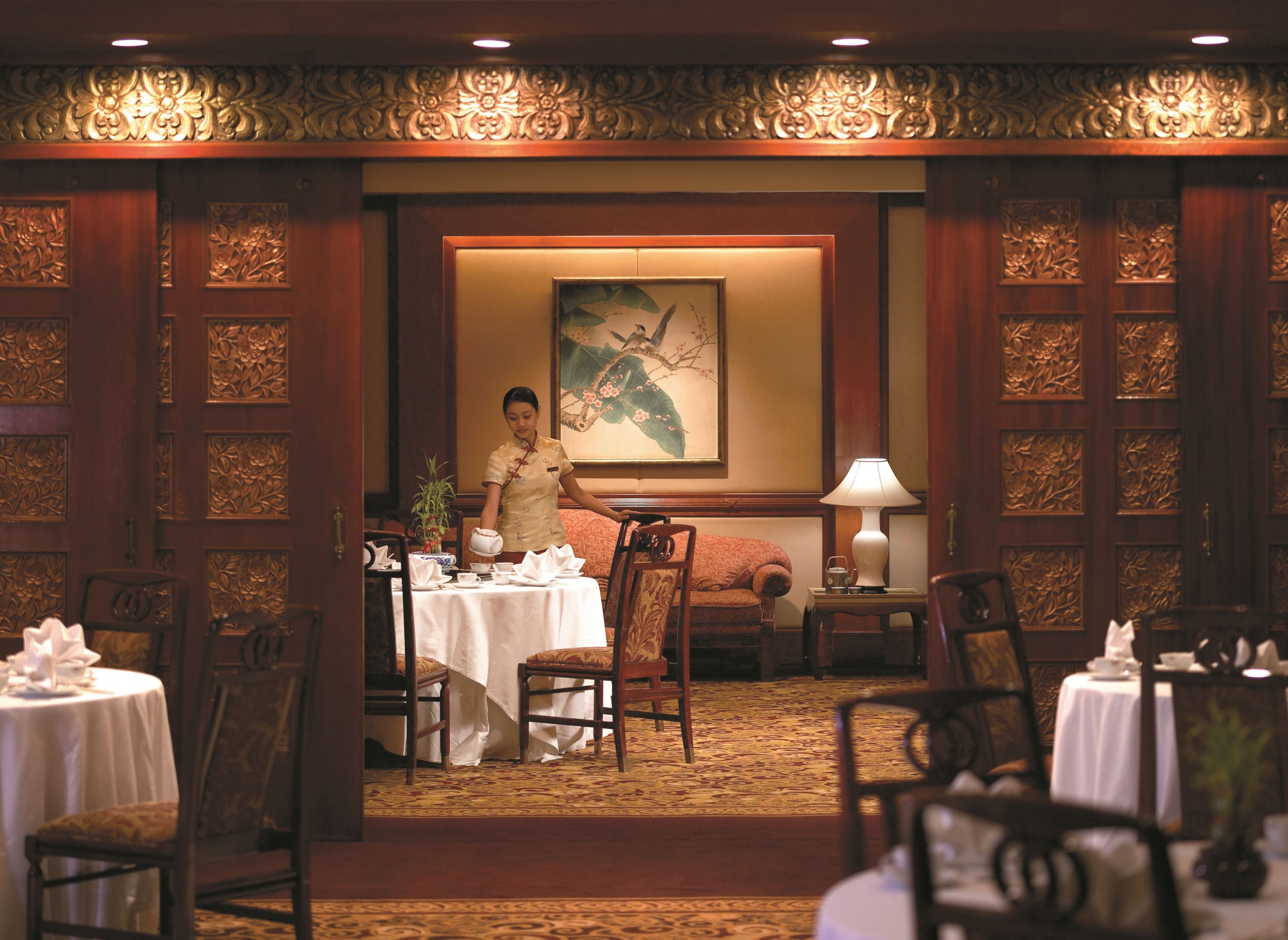 A traditional dining room with ornate wooden paneling, a table set for a meal, and a painting on the wall.