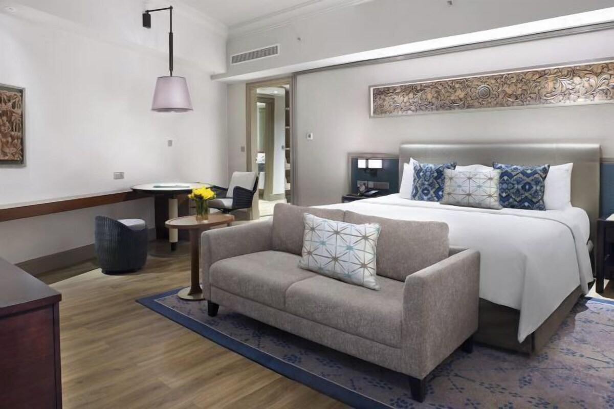 A hotel room with a bed, a sofa, a desk, a lamp, and a decorative wall piece.