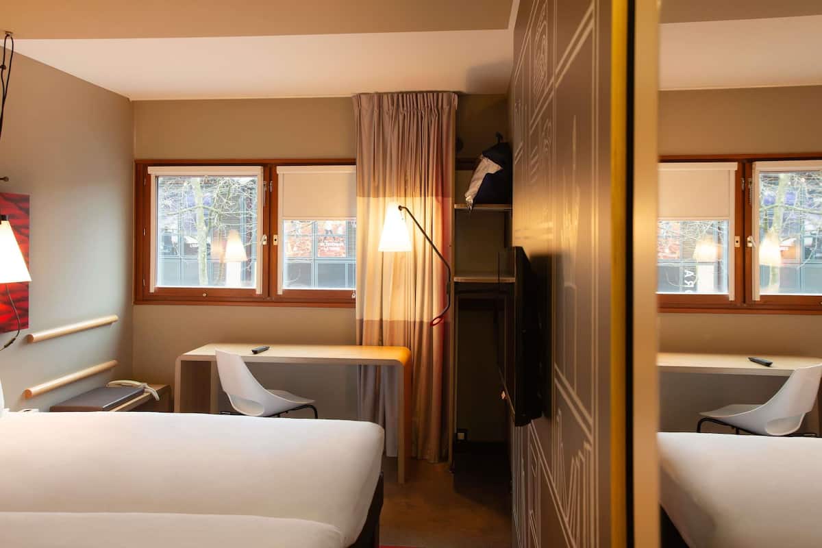Hotellihuone, jossa on kaksi sänkyä, työpöytä, tuoli, televisio ja ikkuna, jossa on verhot.