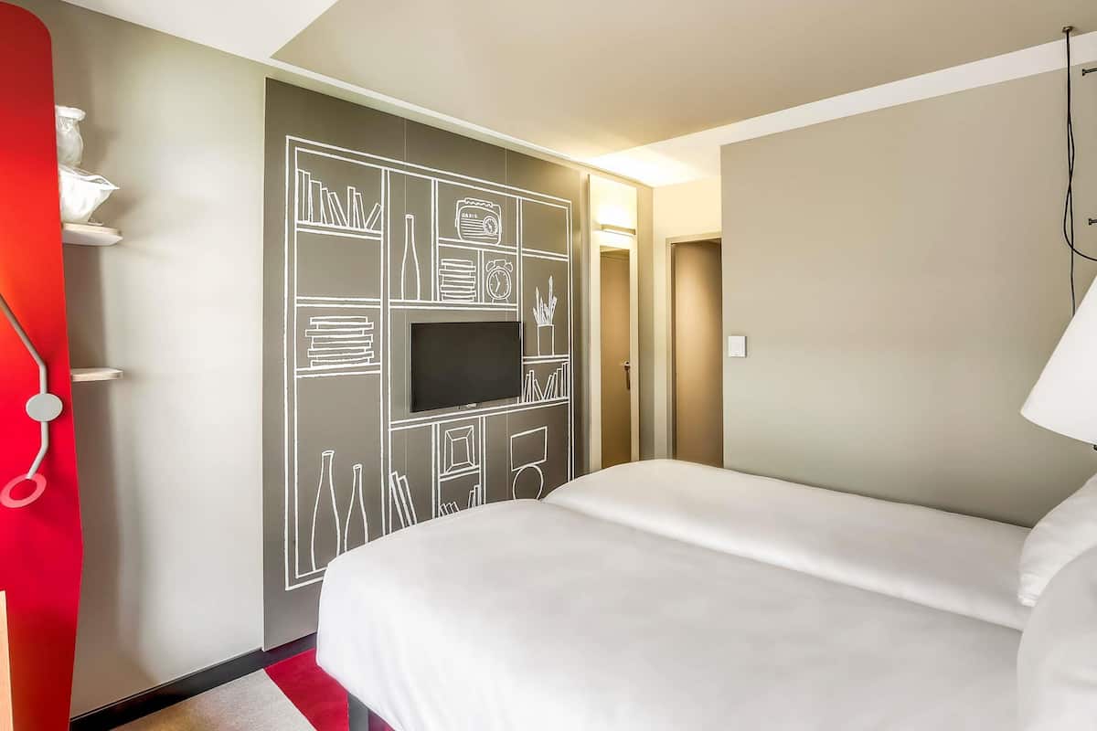 Une chambre d’hôtel avec un lit, un téléviseur fixé au mur et un mur d’accent de couleur rouge.