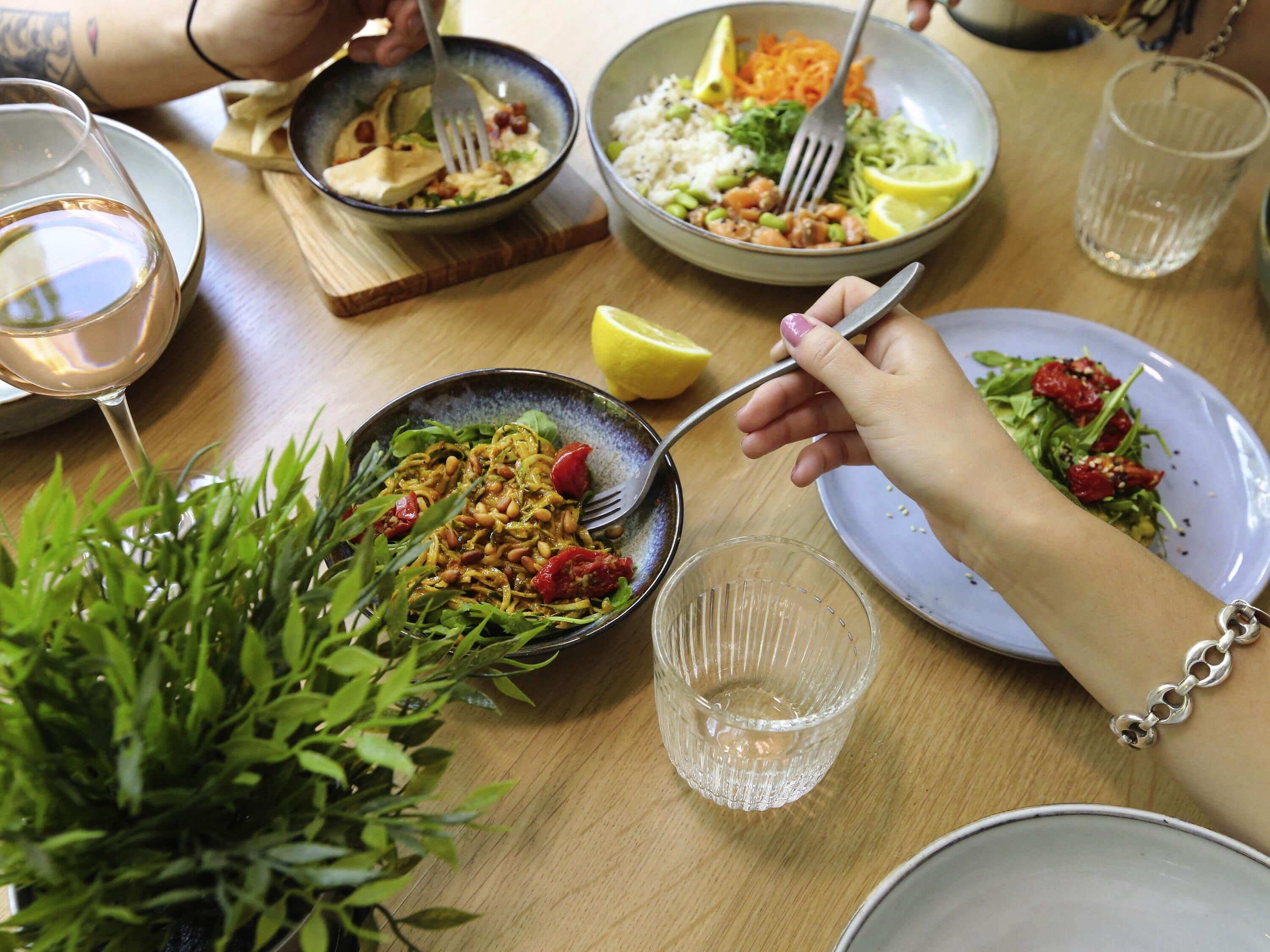 Een eettafel met verschillende gerechten, een glas wijn en een potplant.