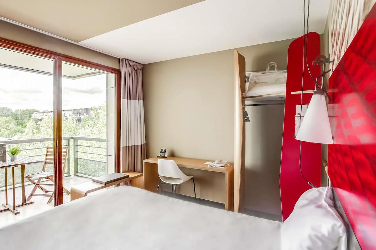 Une chambre d’hôtel avec un lit, un bureau et une chaise, un téléphone et un mur rouge.