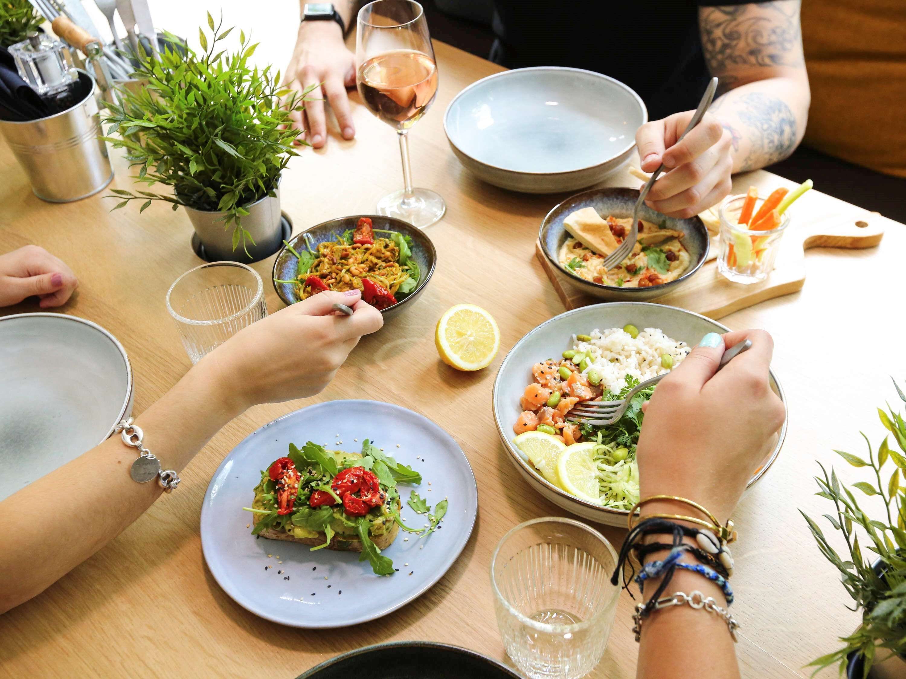 Una mesa de comedor con diversos platos y bebidas, rodeada de gente.