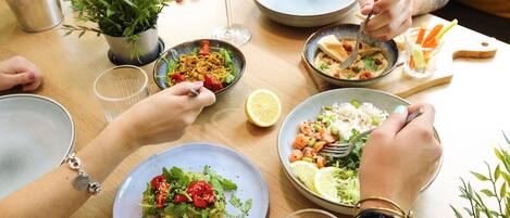 Una mesa de comedor con diversos platos y bebidas, rodeada de gente.