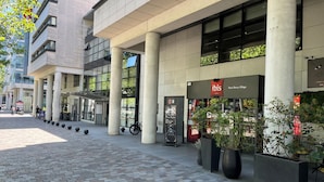 Fachada moderna de hotel con grandes columnas, señalización destacada de 'ibis Paris Bercy Village Hotels' y un paseo pavimentado.