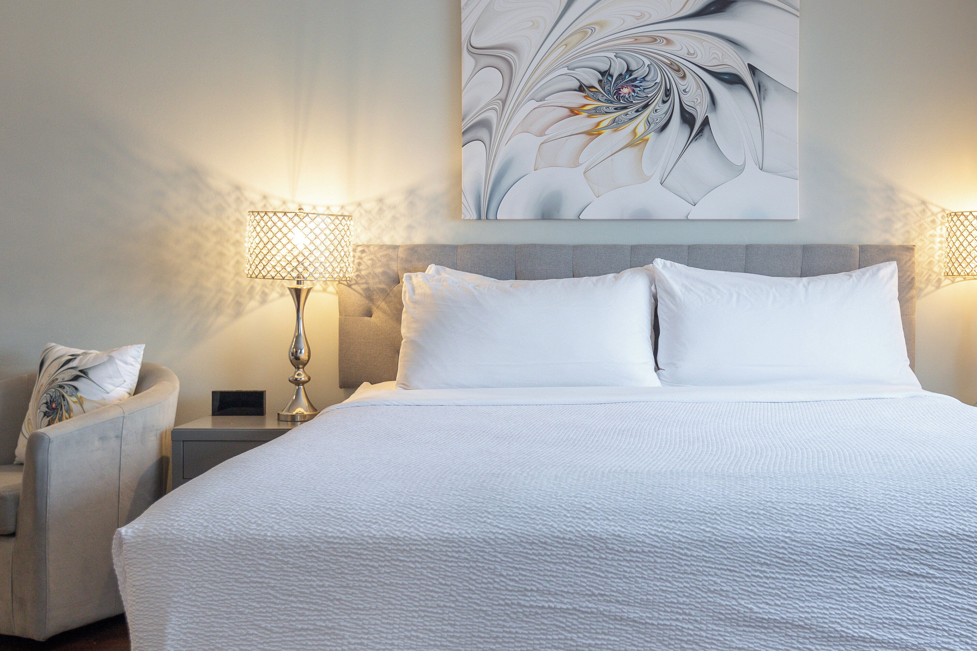 A neatly arranged hotel room with a large bed, two bedside lamps, a chair, and a wall-mounted artwork.
