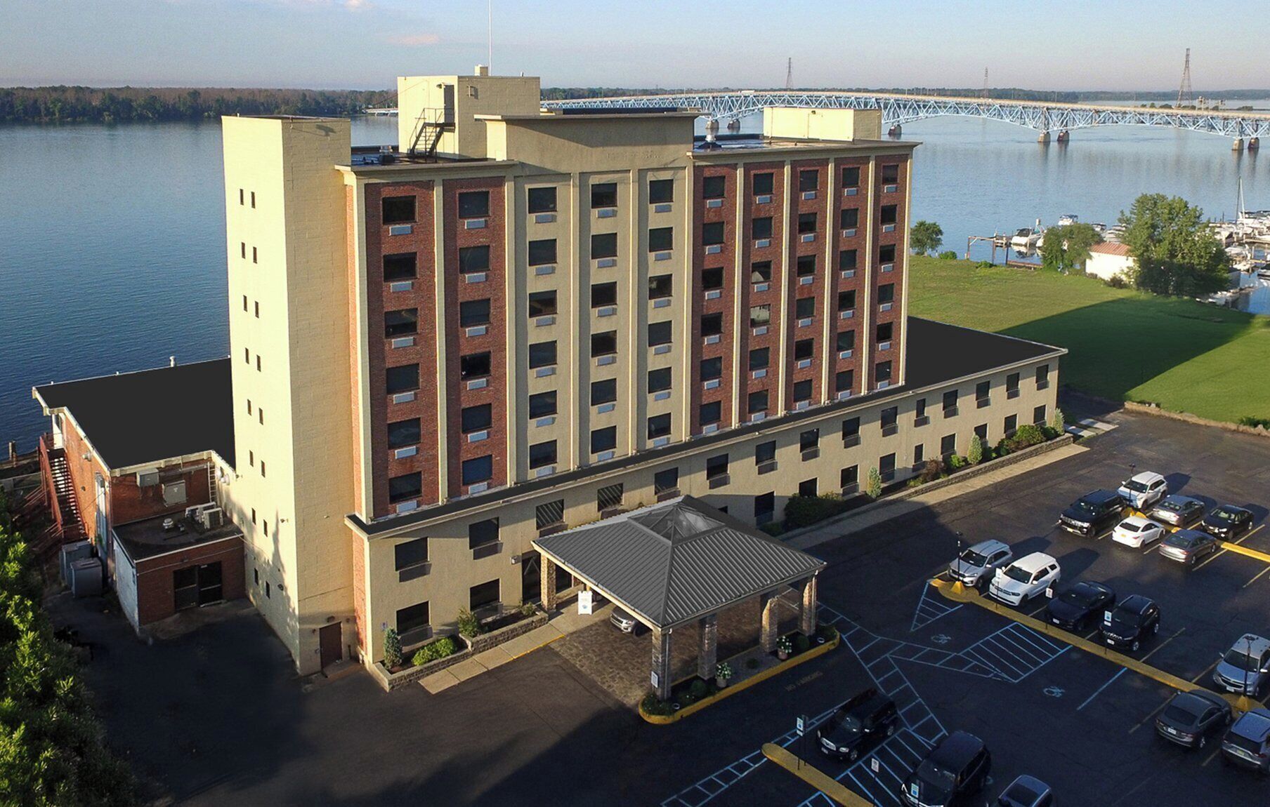 A multi-story hotel with a parking lot and a view of a bridge over a body of water.