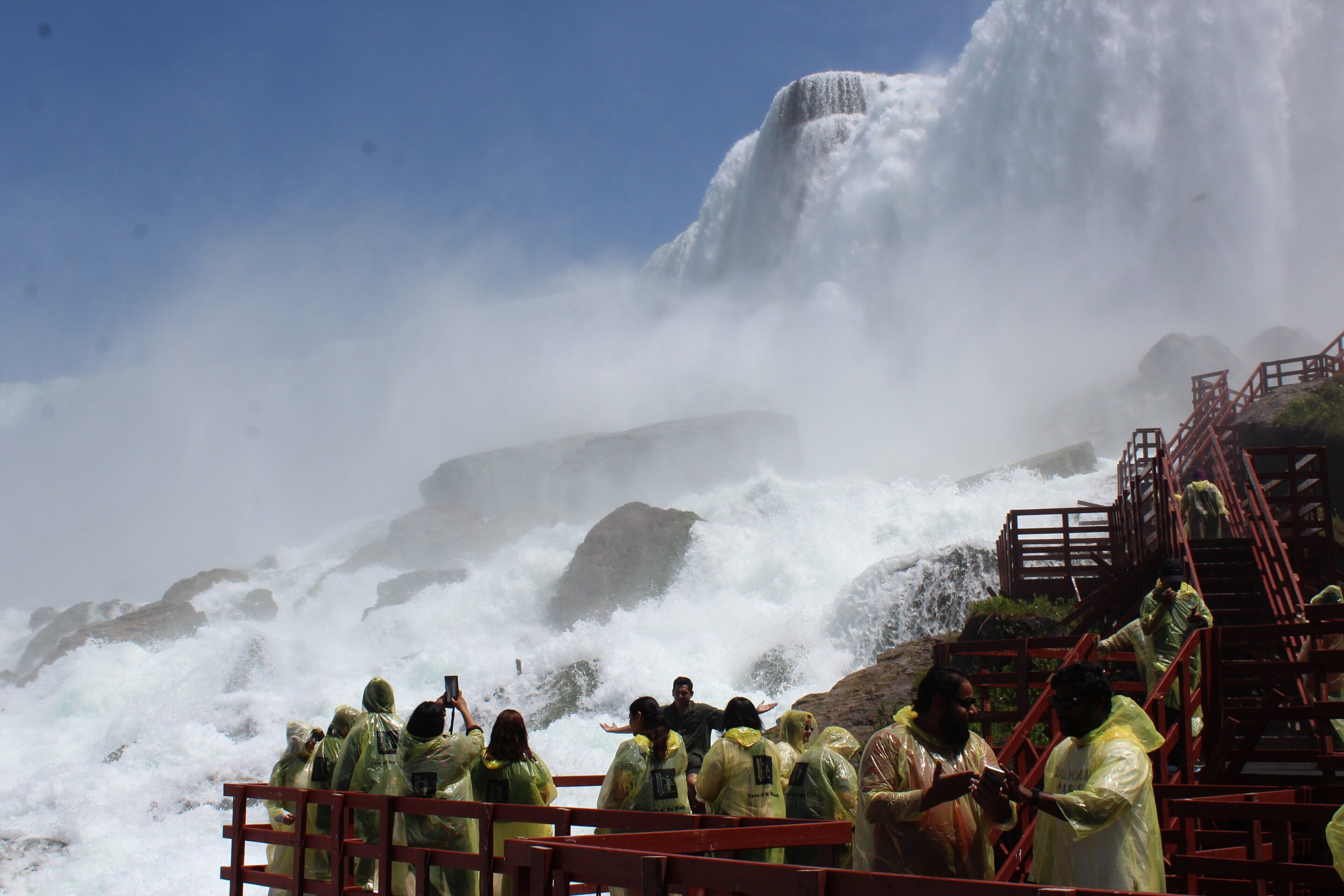 Un grupo de personas observando una cascada con un fondo rocoso y una escalera roja.
