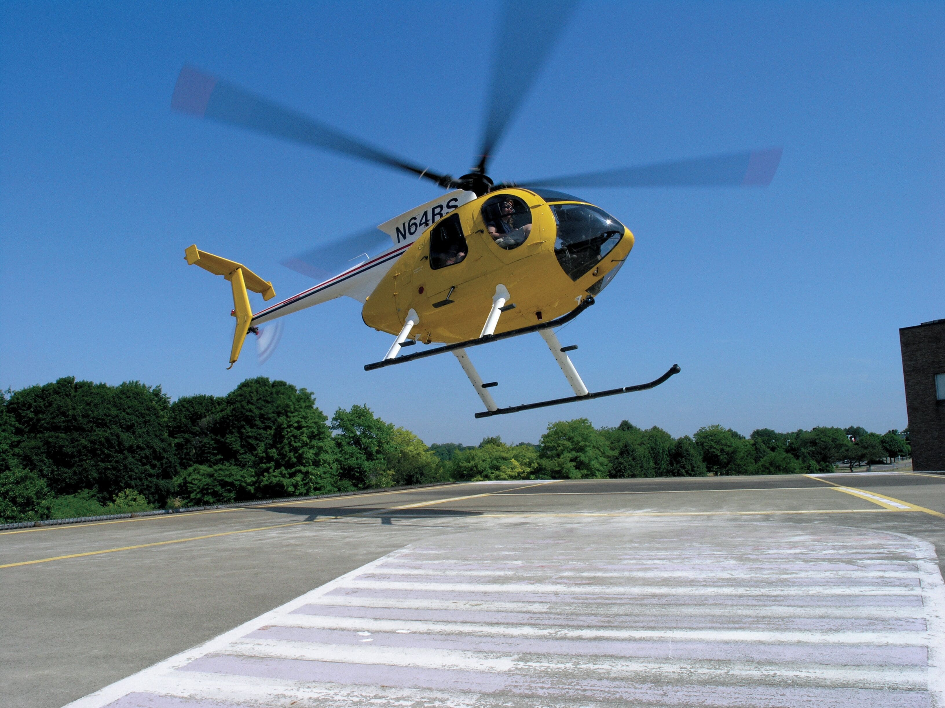 A yellow helicopter with registration N64RS hovering above a marked landing area.