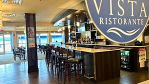Interior de restaurante con barra, asientos y vistas amplias a través de grandes ventanales.