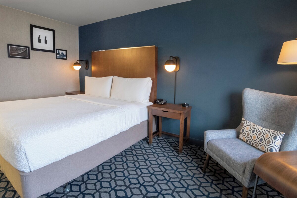 A hotel room with a large bed, bedside tables, a chair, and wall-mounted lamps.