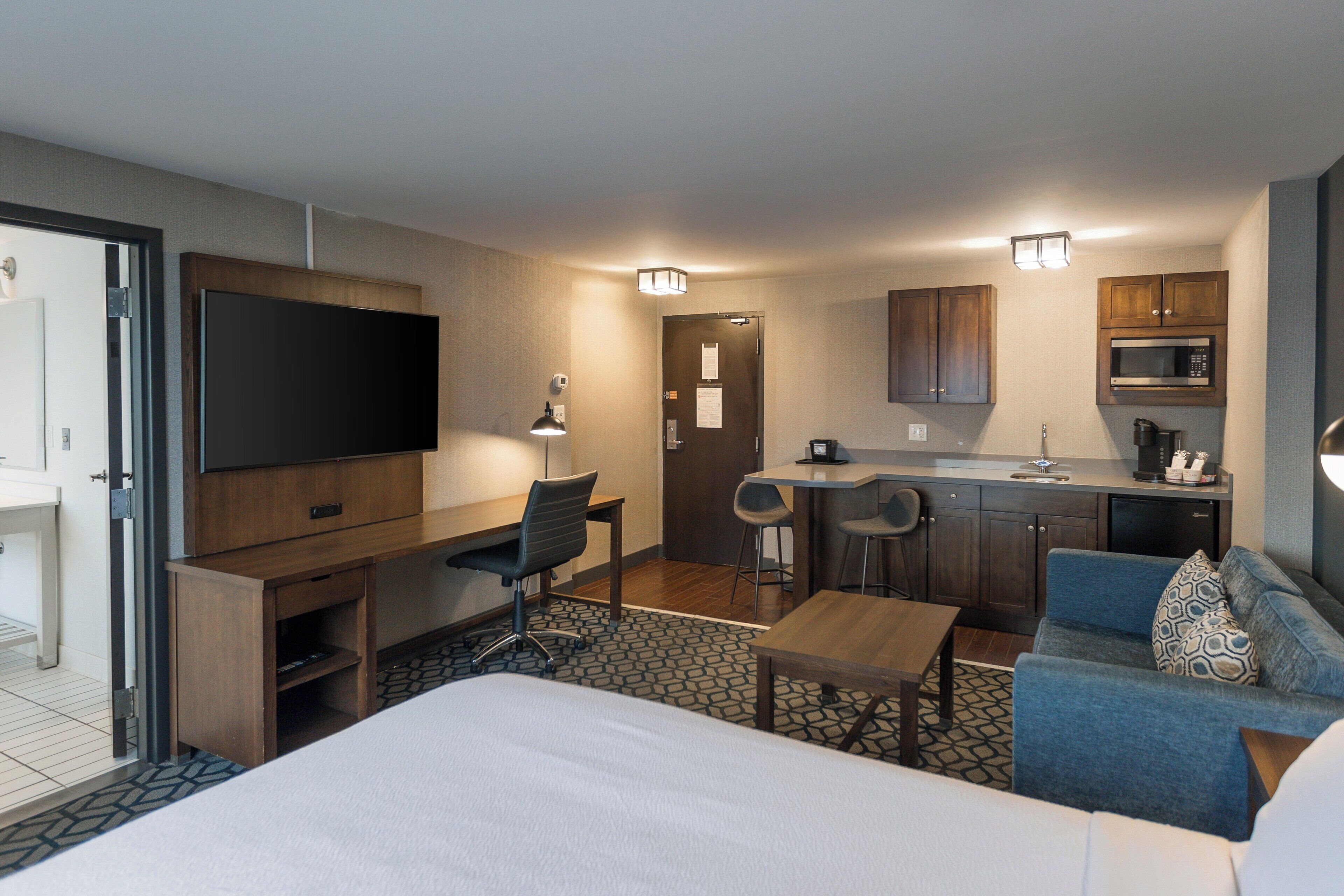 Una habitación de hotel con una cama, un escritorio con una silla, una kitchenette, un sofá y un televisor.