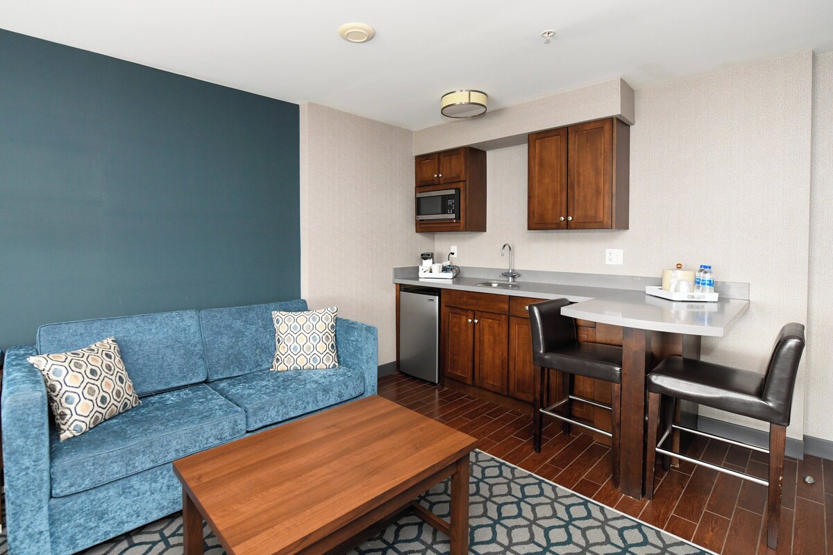 A compact living space with a kitchenette, a blue sofa with patterned cushions, a wooden coffee table, and a patterned rug.
