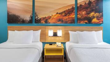 Habitación de hotel con dos camas, cabecera de madera, mesita de noche con teléfono, y pared decorada con tres pinturas de paisajes otoñales.