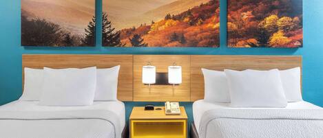 Habitación de hotel con dos camas, cabecera de madera, mesita de noche con teléfono, y pared decorada con tres pinturas de paisajes otoñales.