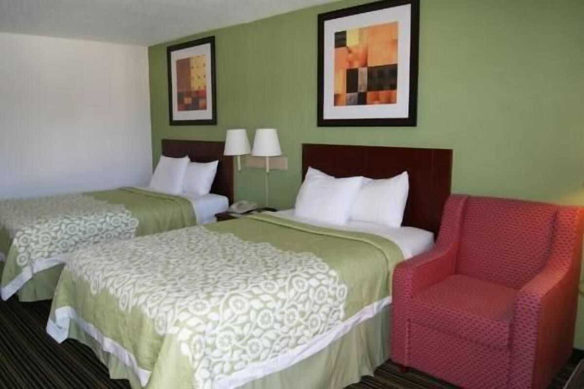 Habitación de hotel con dos camas, un sillón rojo y dos cuadros en la pared.