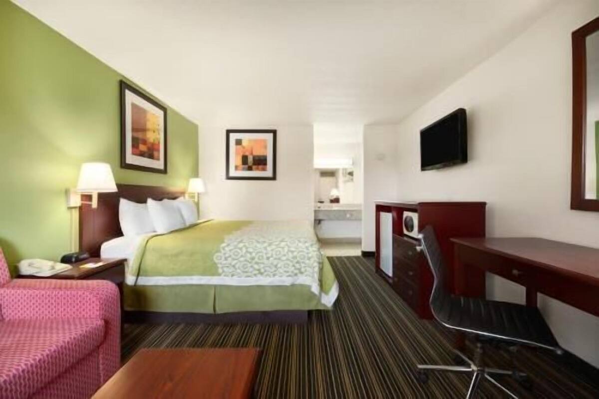Habitación de hotel con cama, escritorio, silla, televisor y baño a la vista.