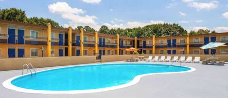 Una piscina con sillas de descanso y sombrillas, rodeada por un edificio con varios balcones y ventanas.