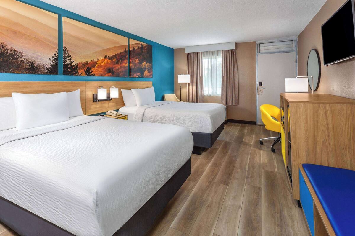 Habitación de hotel con dos camas, un escritorio, una silla, un televisor y un cuadro en la pared.