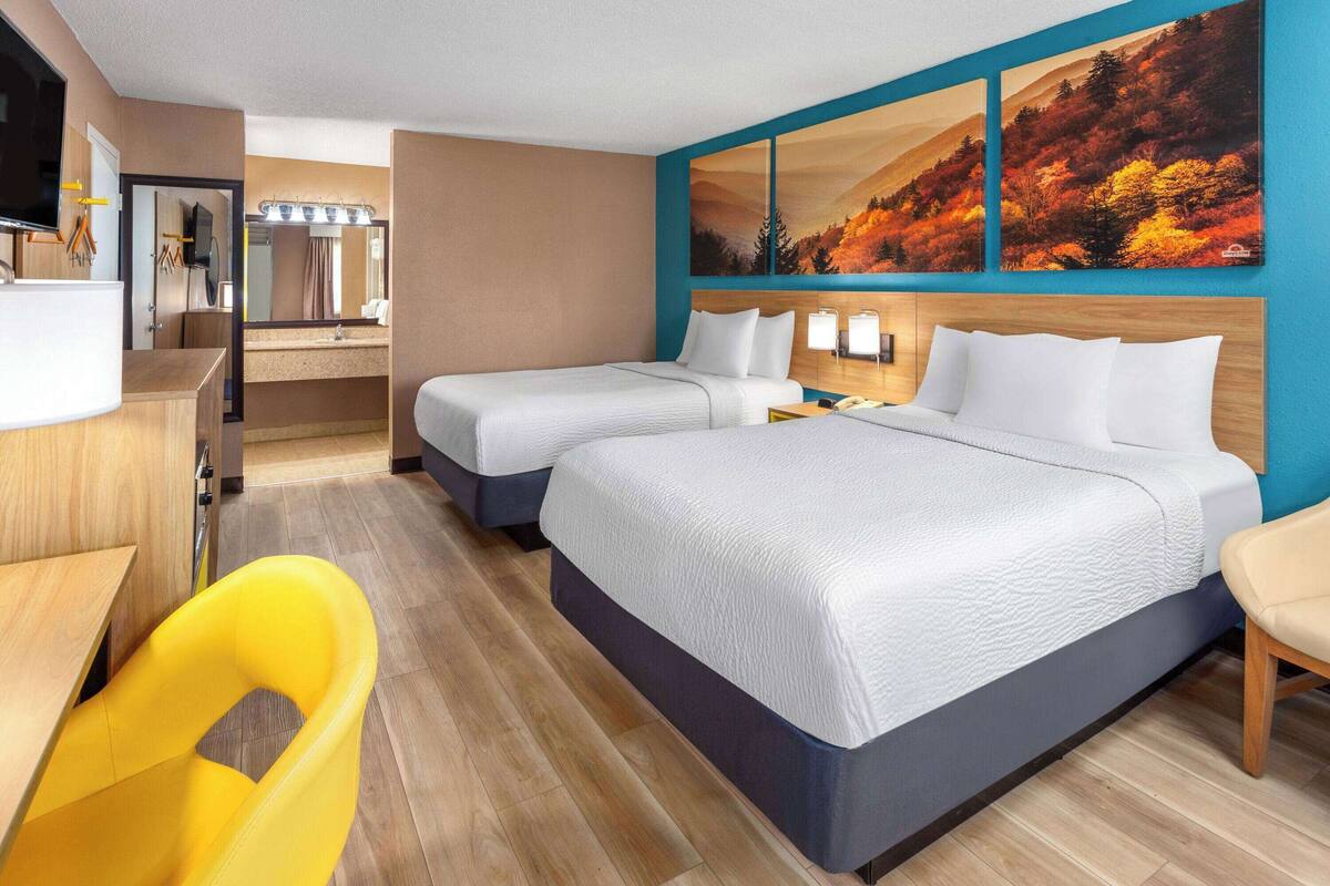 Habitación de hotel con dos camas, un escritorio, una silla, baño y un cuadro grande en la pared.